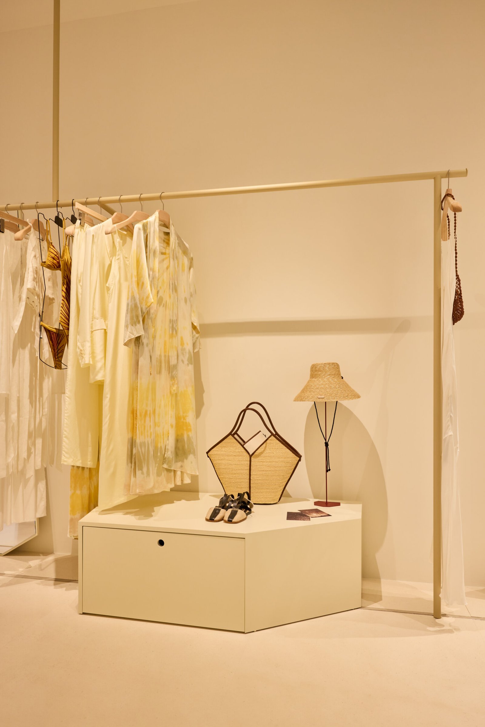 Escaparate de moda con prendas amarillas colgadas y accesorios sobre un mueble blanco